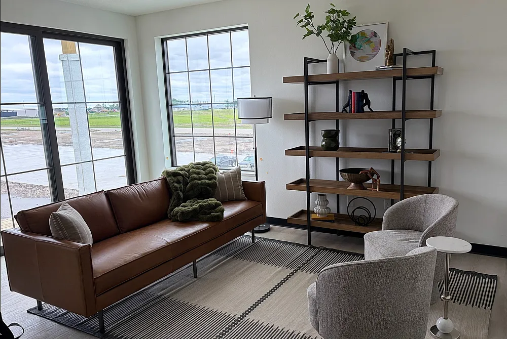Bright and cozy living room with modern brown leather sofa, elegant shelving, and panoramic windows offering scenic views.