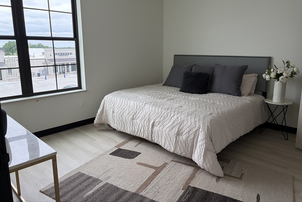 Bright and inviting bedroom with a cozy bed, stylish pillows, and a decorative bedside table, showcasing modern interior design and a large window view.