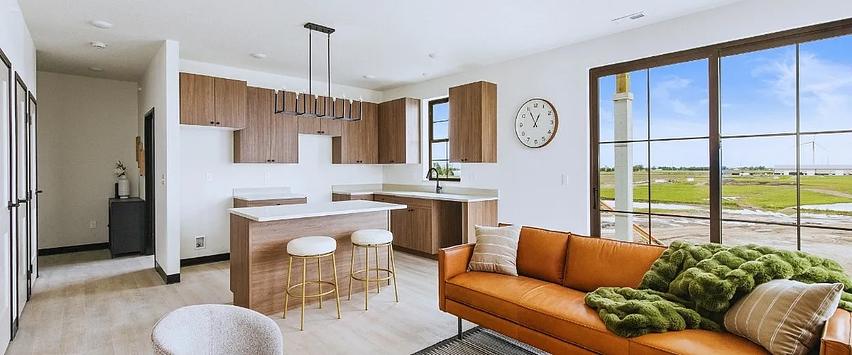 Modern open-concept living space with sleek kitchen, cozy sofa, and expansive windows overlooking vibrant greenery.