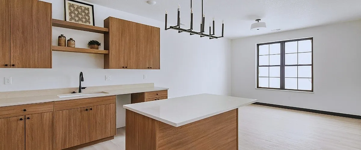 Modern kitchen with elegant wooden cabinets, sleek island, and stylish chandelier in a bright, sunlit room.