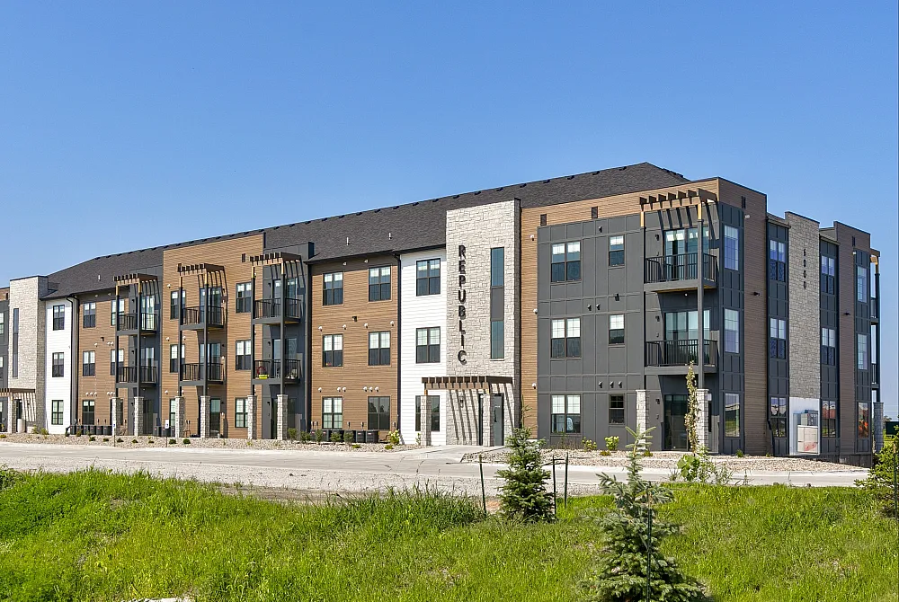 Modern apartment complex with stylish architecture set against a clear blue sky, featuring multiple balconies and landscaped greenery.