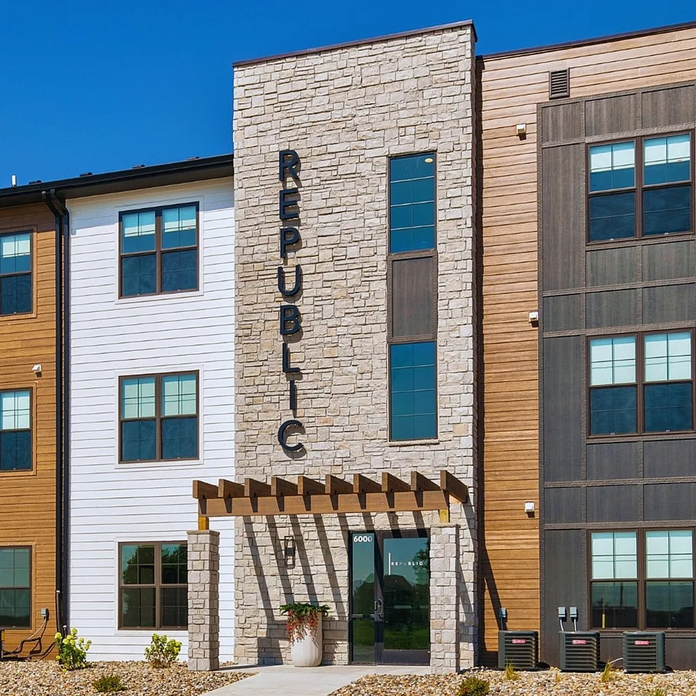 Modern apartment building with elegant stone fa&ccedil;ade and wood paneling, featuring stylish entrance and large windows for natural light.