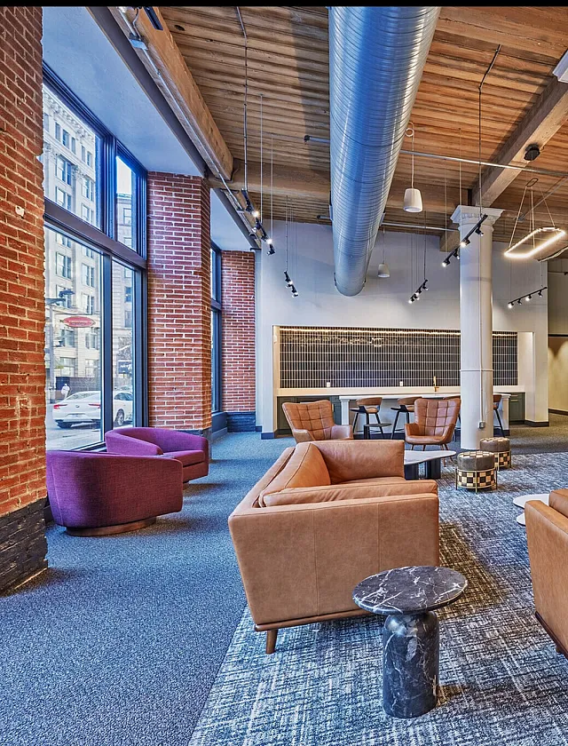 Modern industrial-style lounge with exposed brick, plush seating, and sleek kitchen area featuring green cabinetry and contemporary lighting.