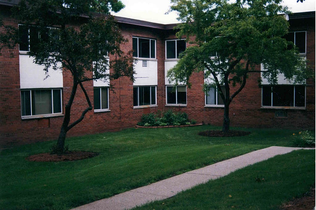 Charming apartment exterior with lush green lawn and mature trees, perfect for a serene living environment.