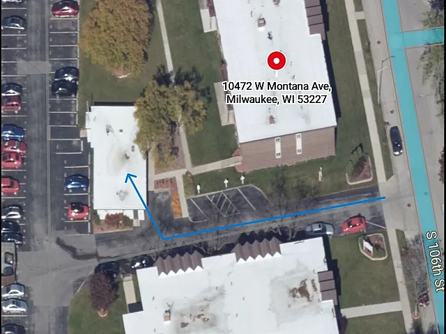 Aerial view of a well-maintained white-roof building with adjacent parking and lush greenery at 10472 W Montana Ave, Milwaukee, WI. Convenient urban access with clear pathways and ample parking spaces.