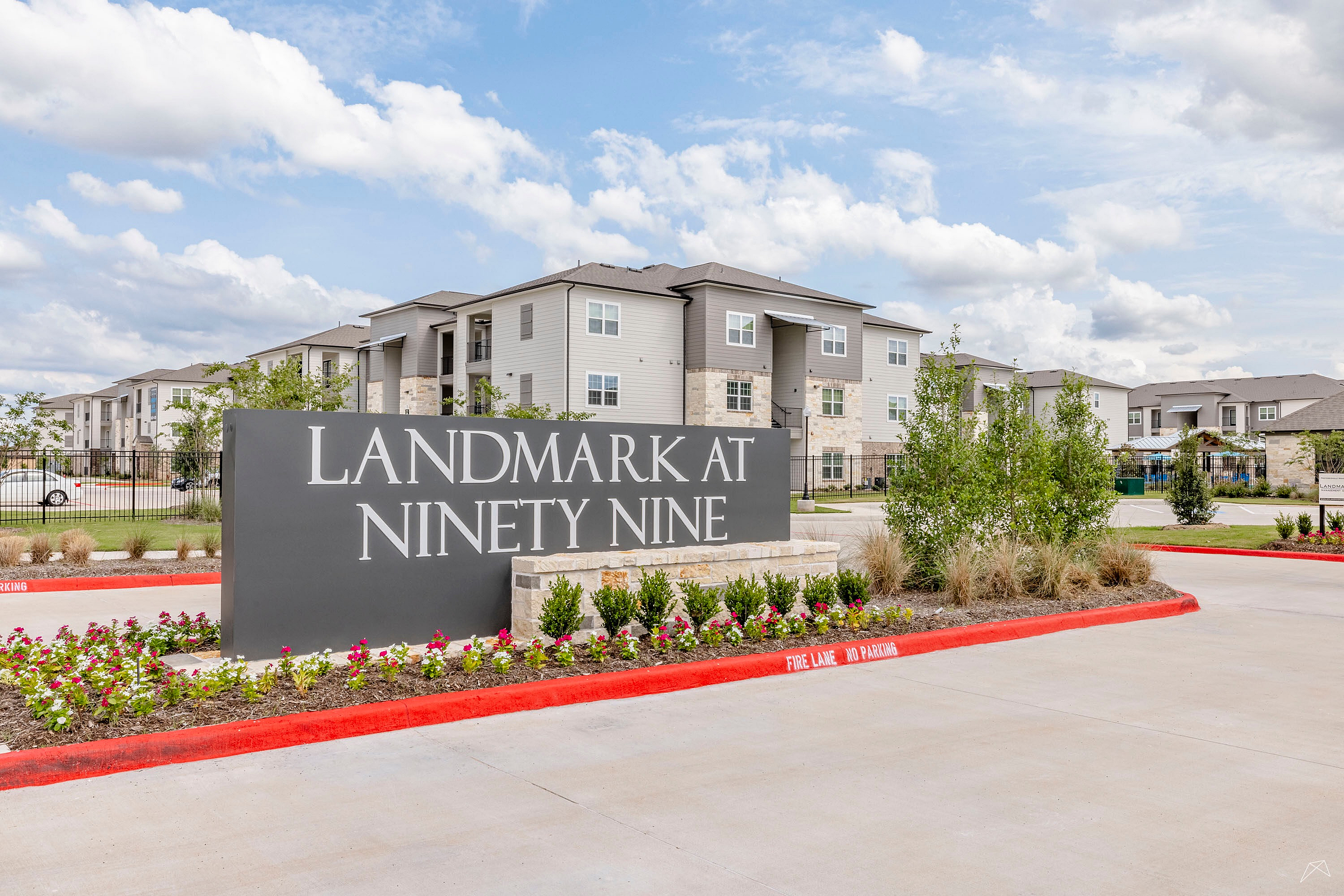 Chic exterior view of Landmark at Ninety Nine apartments with inviting landscaping and modern architecture set against a vibrant blue sky.
