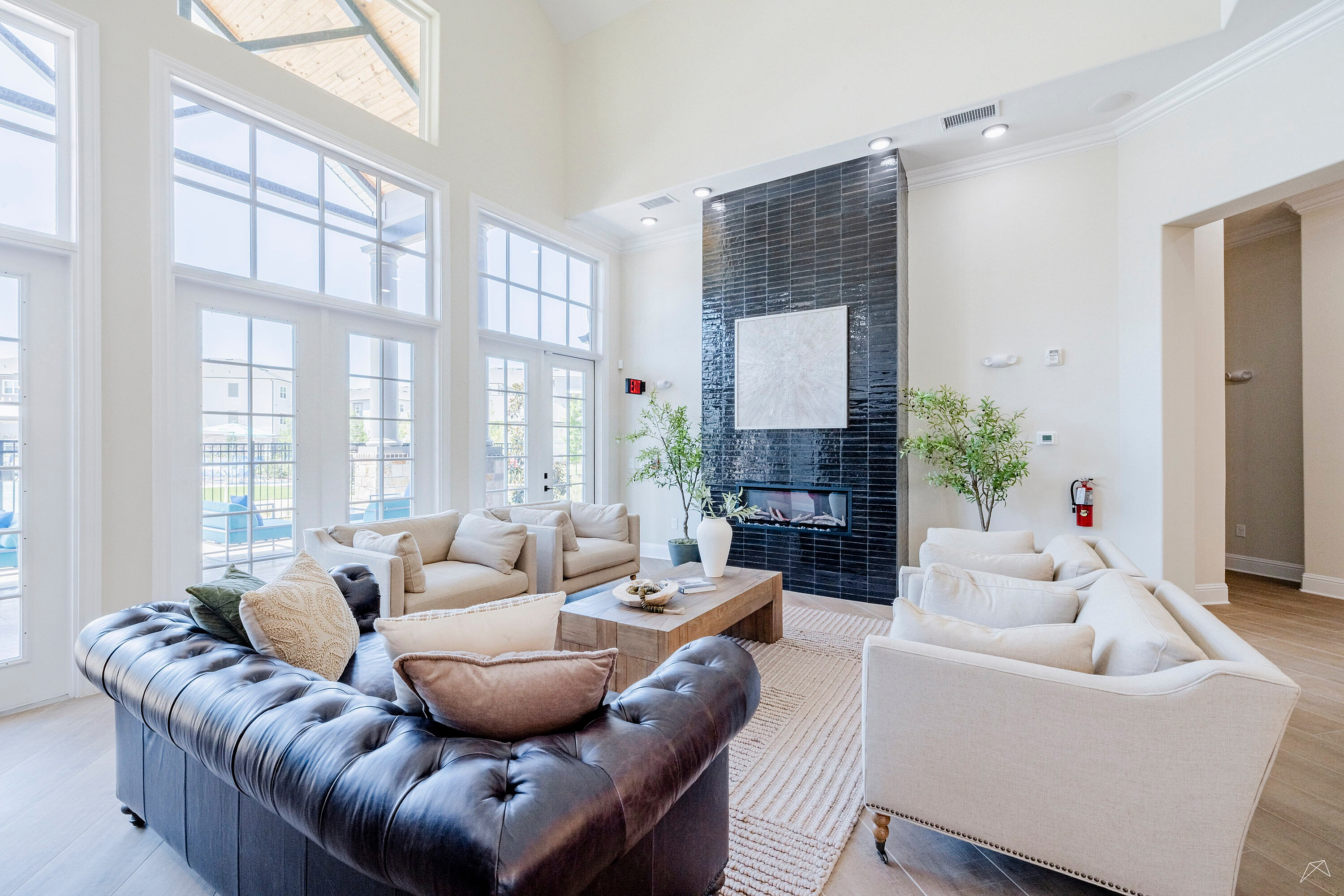 Luxurious living room with high ceilings, elegant sofas, and a modern fireplace, overlooking a sunlit patio through expansive windows.