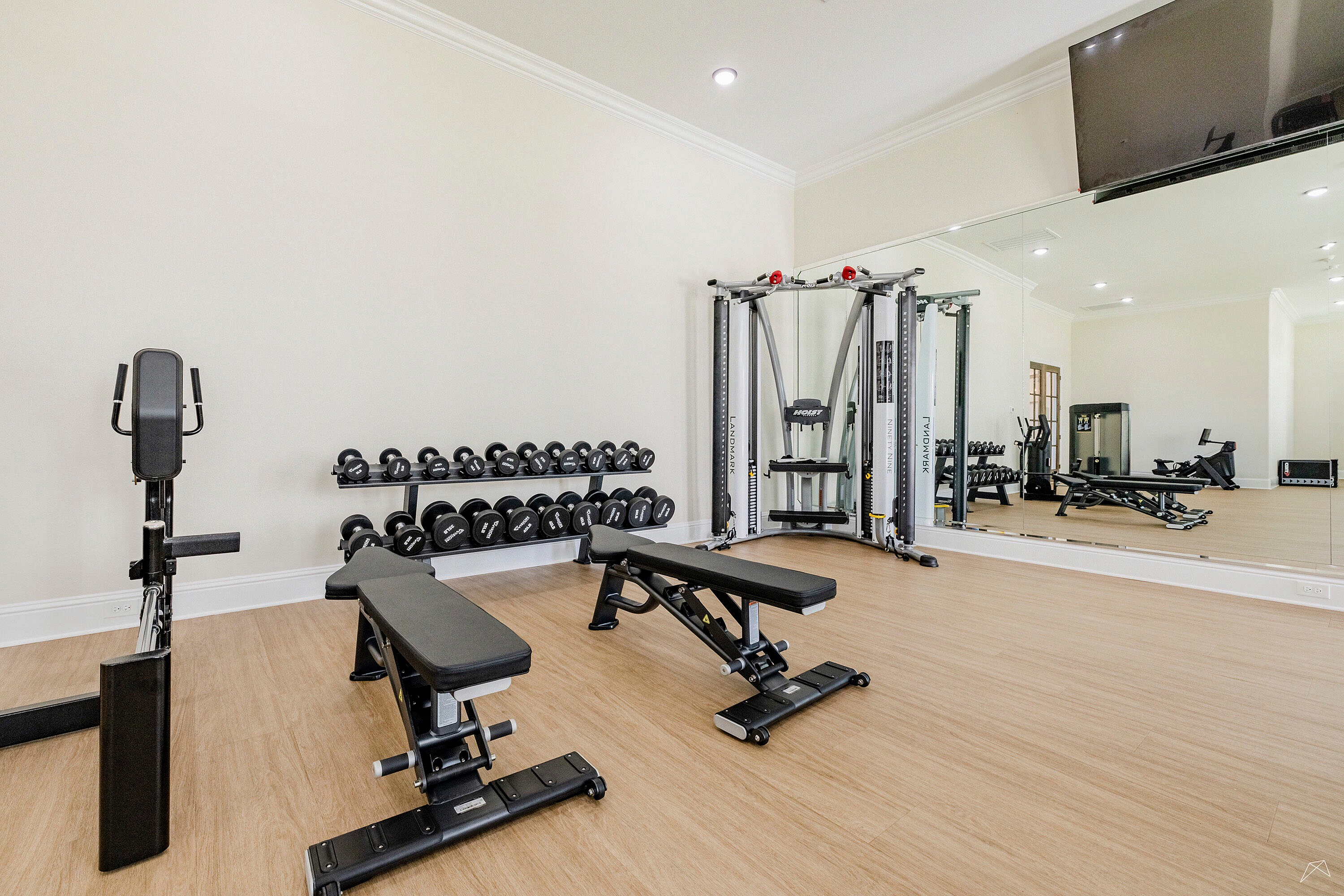 Modern fitness center with sleek wooden floors, complete with exercise machines and free weights, offering a stylish workout environment.