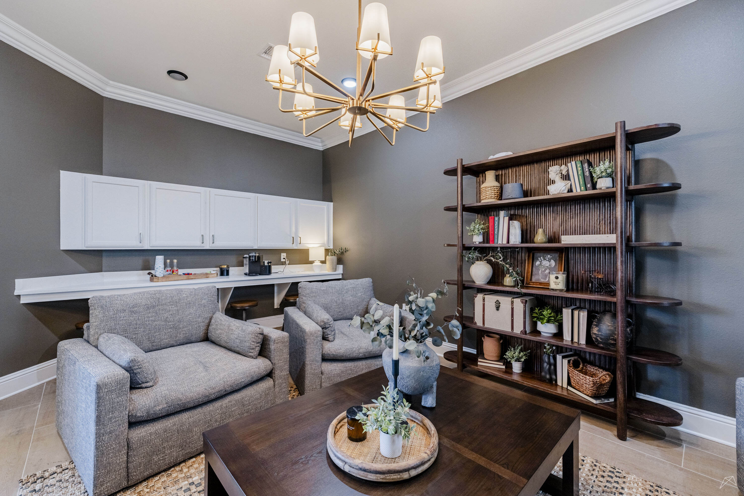Modern living area with elegant lighting, cozy gray chairs, and stylish open shelving showcasing books and decor.