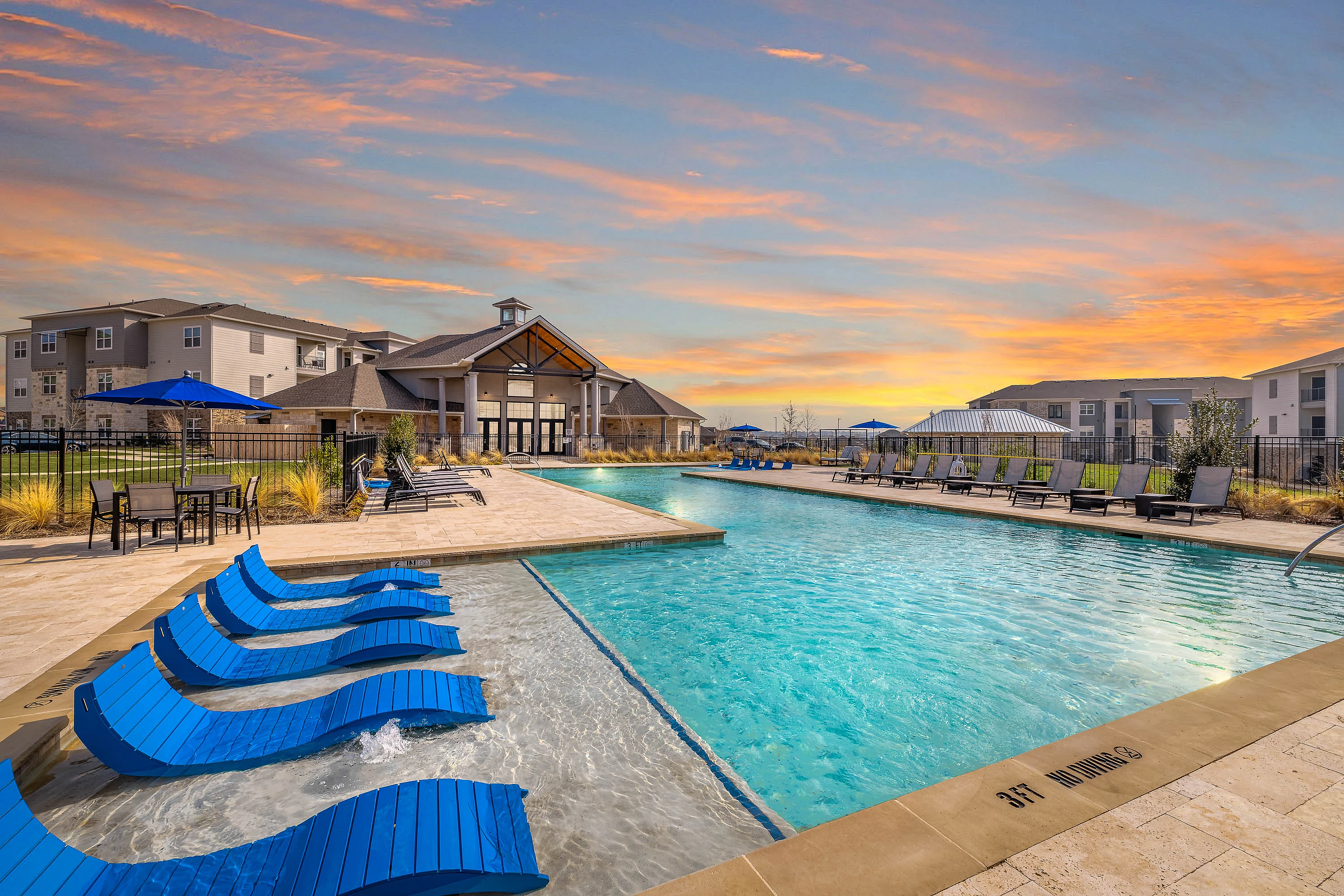 Luxurious apartment community with a stunning outdoor pool, modern lounge chairs, sundeck, outdoor kitchen, and lush greenery.