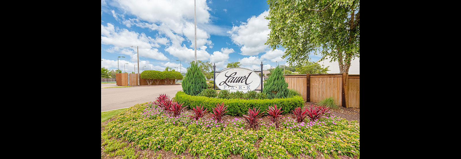 Entrance to Laurel Park featuring a beautifully landscaped garden with vibrant flowers and lush greenery under a clear sky.
