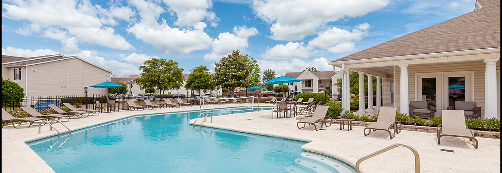 Inviting outdoor pool area with sun loungers and shaded seating, surrounded by lush greenery and villa-like buildings.