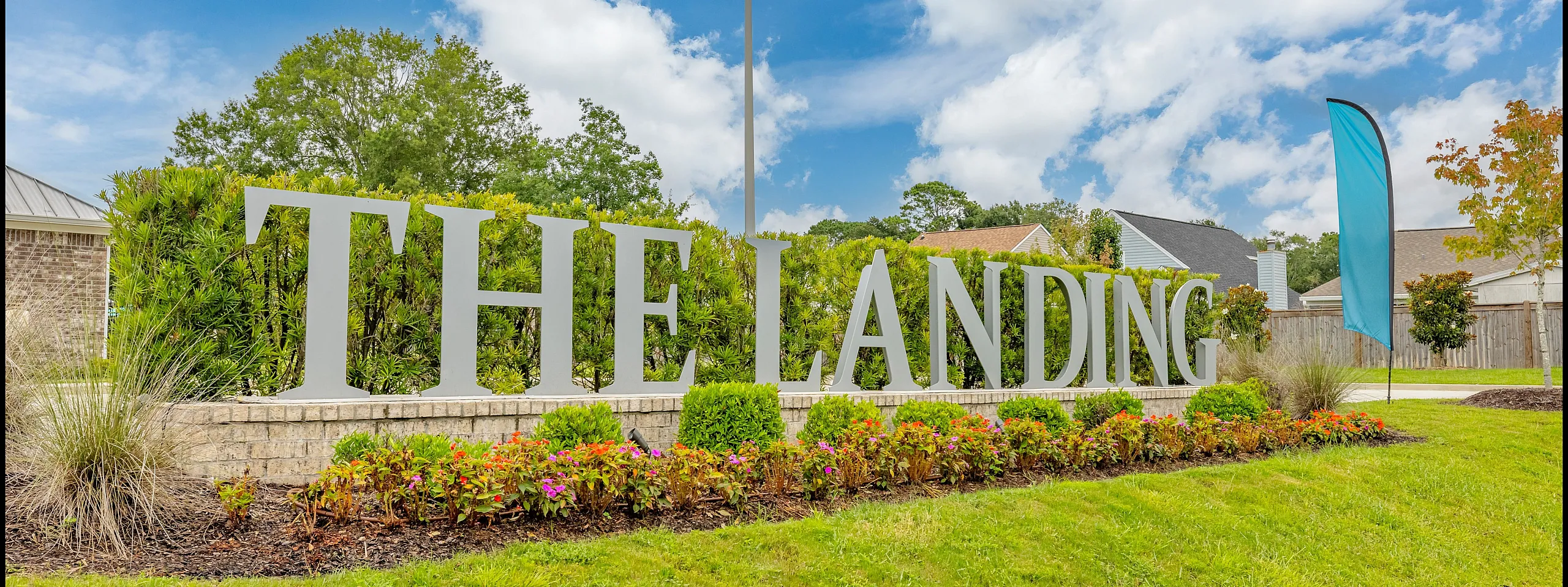 Inviting entrance sign of The Landing with vibrant landscaping and a clear blue sky.