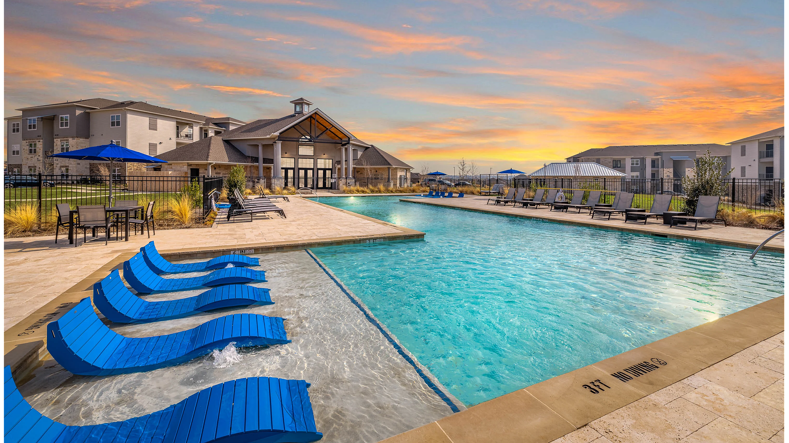 Stunning apartment complex with a stylish pool area, lounge chairs, and a beautiful sunset backdrop.
