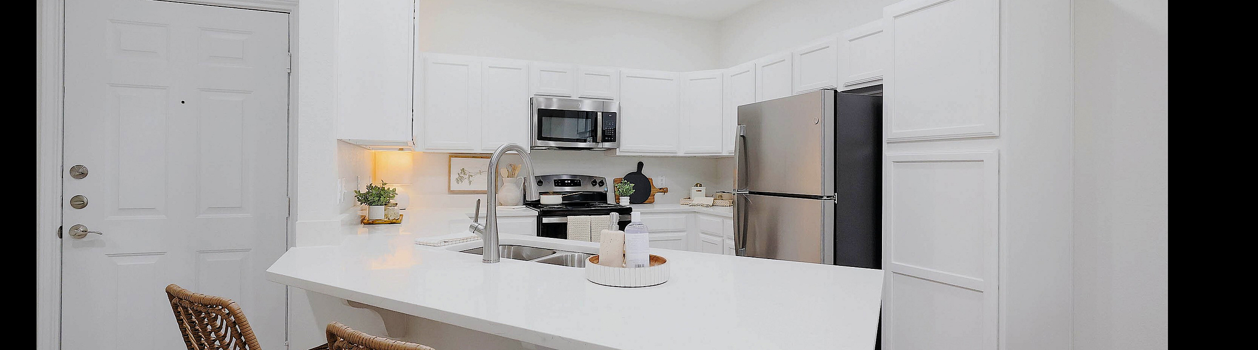 Bright modern kitchen with sleek white cabinetry, stainless steel appliances, and a chic breakfast bar with stylish wicker stools.