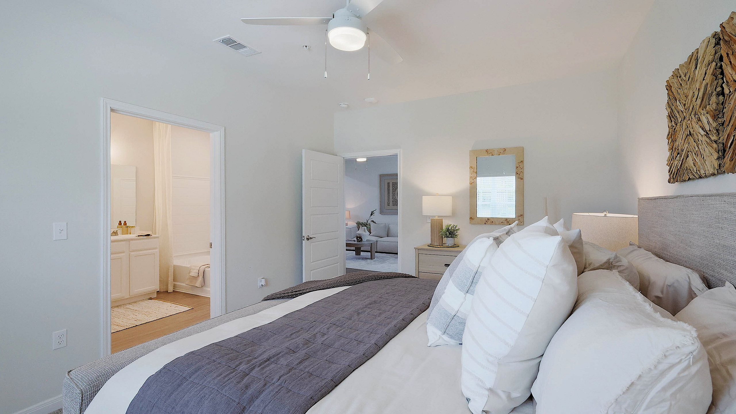 Inviting bedroom with plush bedding and natural light, leading to a chic en-suite bathroom and cozy living room.