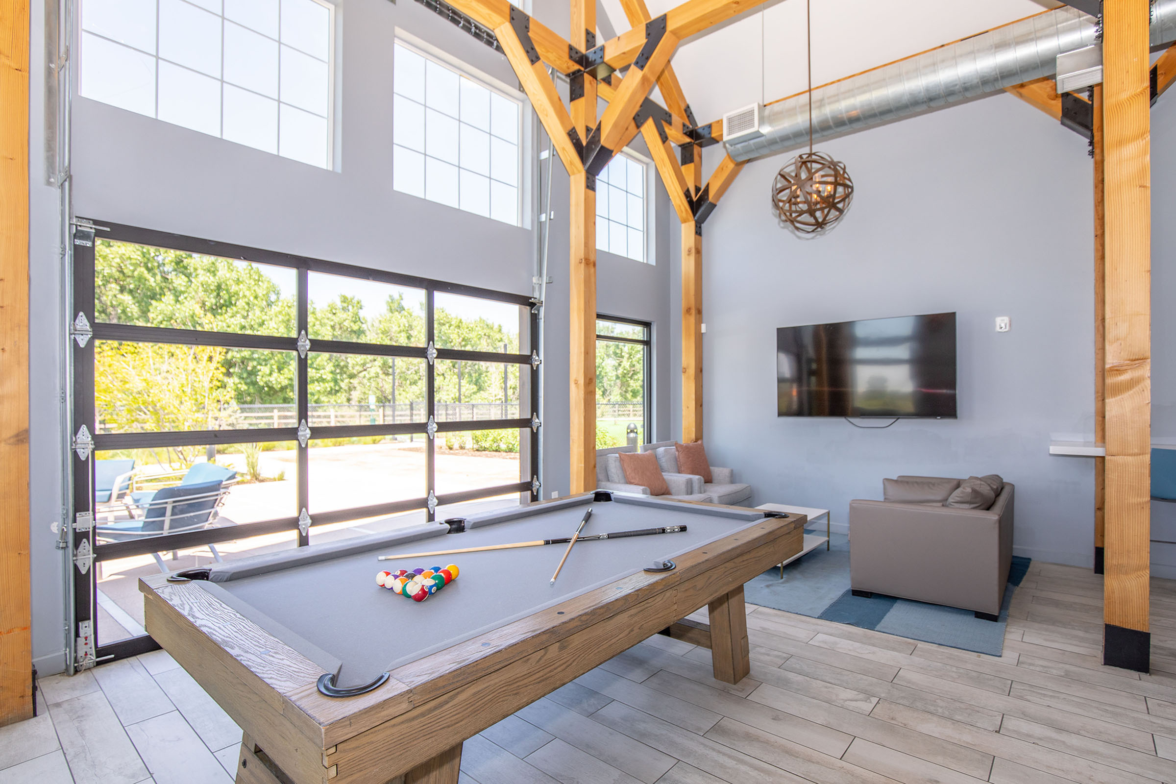Modern lounge featuring a stylish billiards table, comfortable seating area, and large windows with abundant natural light.