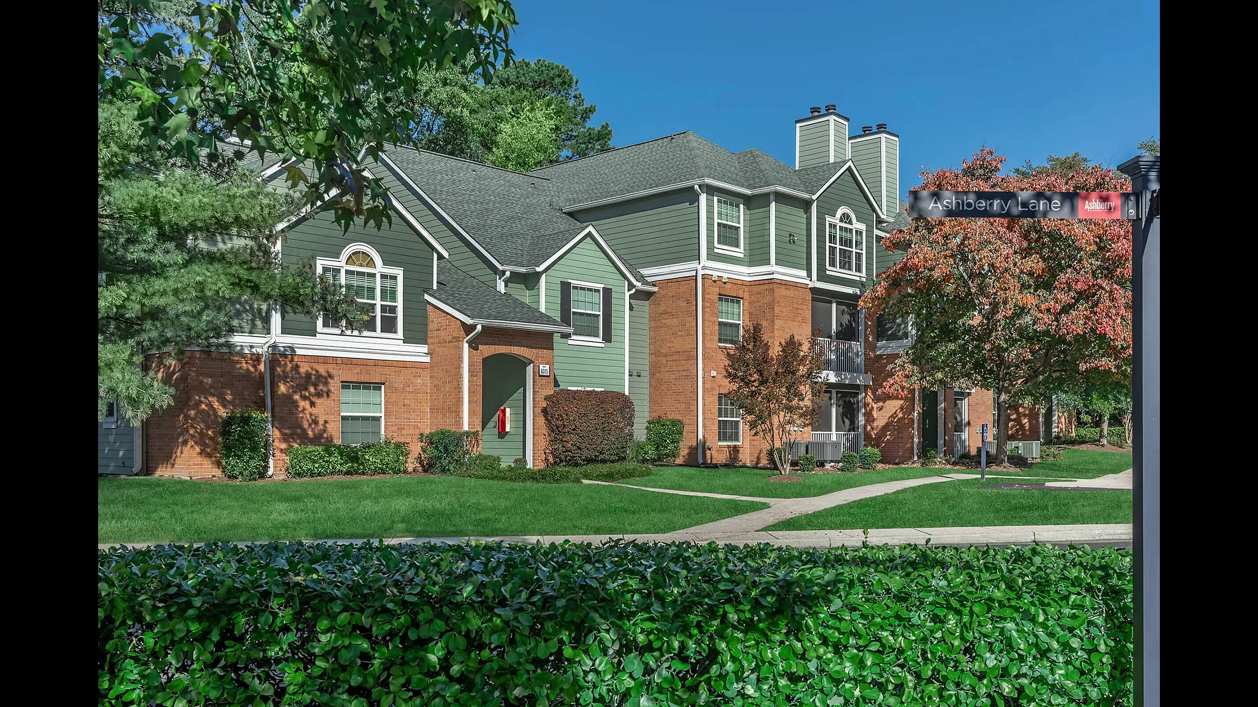 The Ashberry Apartment Homes Building Exterior with Brick and Green Siding and Lush Landscaping