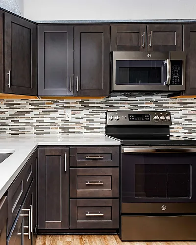 The Ashberry Apartment Homes Kitchen with Modern Dark Cabinets, Stainless Steel Appliances, Tile Backsplash, Quartz Countertops and Wood Plank Flooring