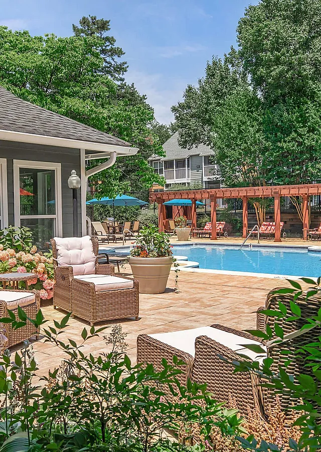 The Ashberry Apartment Homes Swimming Pool with Lounge Seating, Pergola with Loungers, Blue Umbrellas and Lush Landscaping