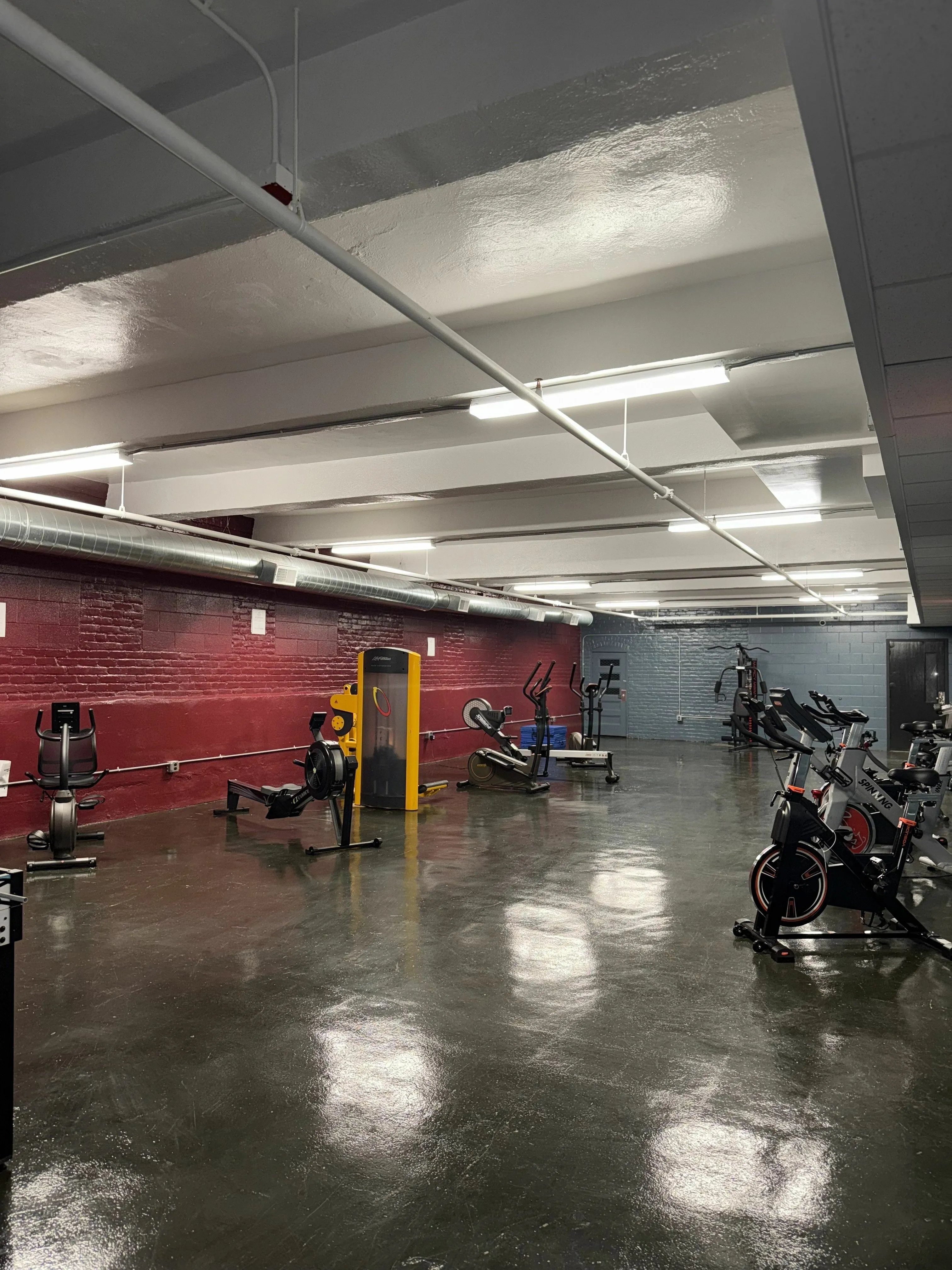 Spacious fitness center featuring modern exercise machines and sleek industrial design. Chic recreational area with a vibrant foosball table and modern wall-mounted TV, ideal for entertainment and relaxation.
