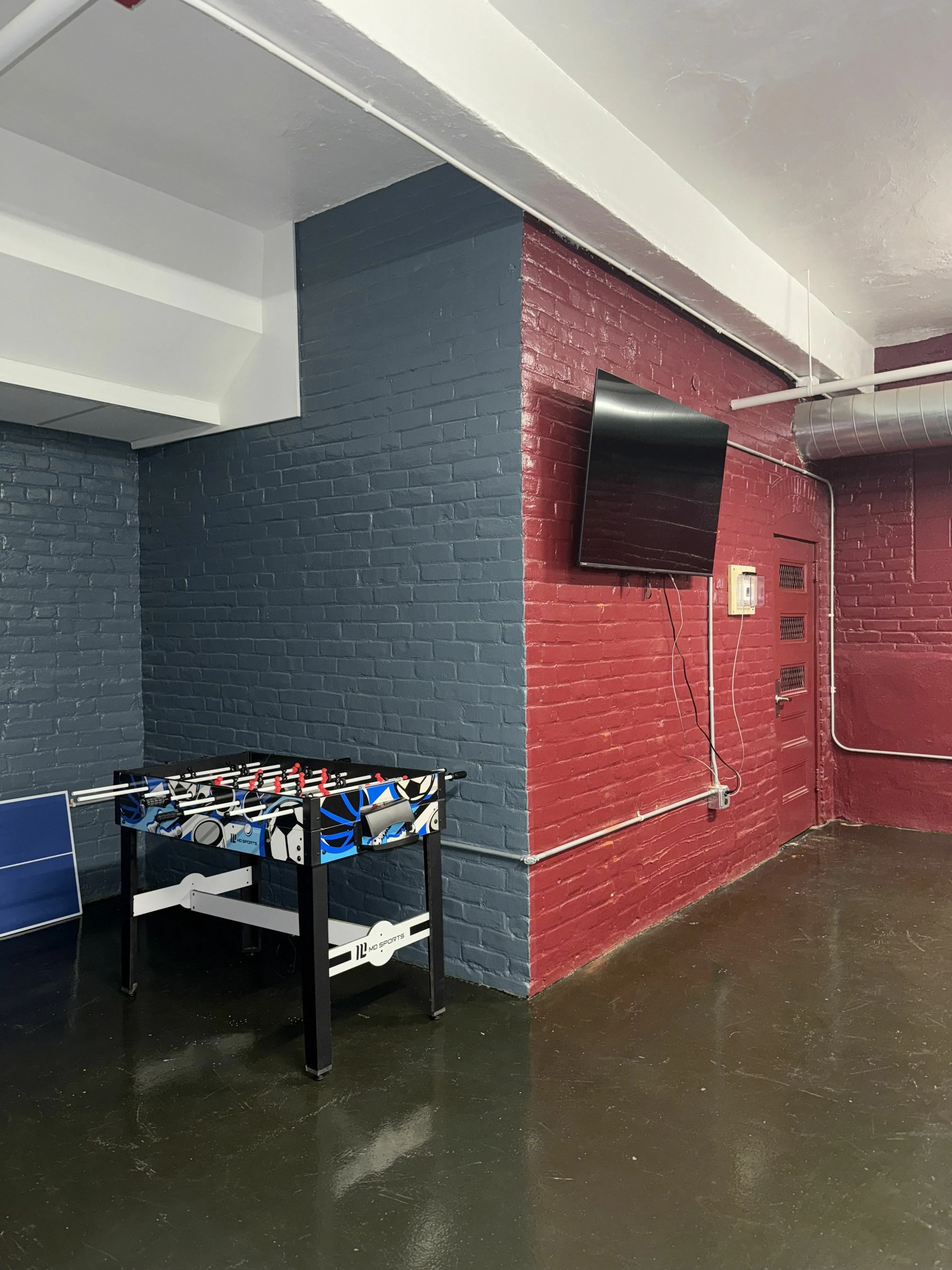 Chic recreational room with a vibrant foosball table and modern wall-mounted TV, ideal for entertainment and relaxation.