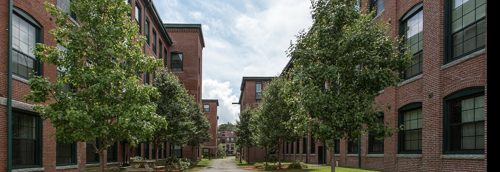 Charming brick apartment complex with lush green landscaping and a welcoming pathway.