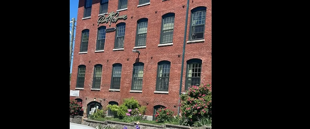 Charming brick apartment building with classic architecture, surrounded by lush greenery and vibrant flowers, perfect for urban living.