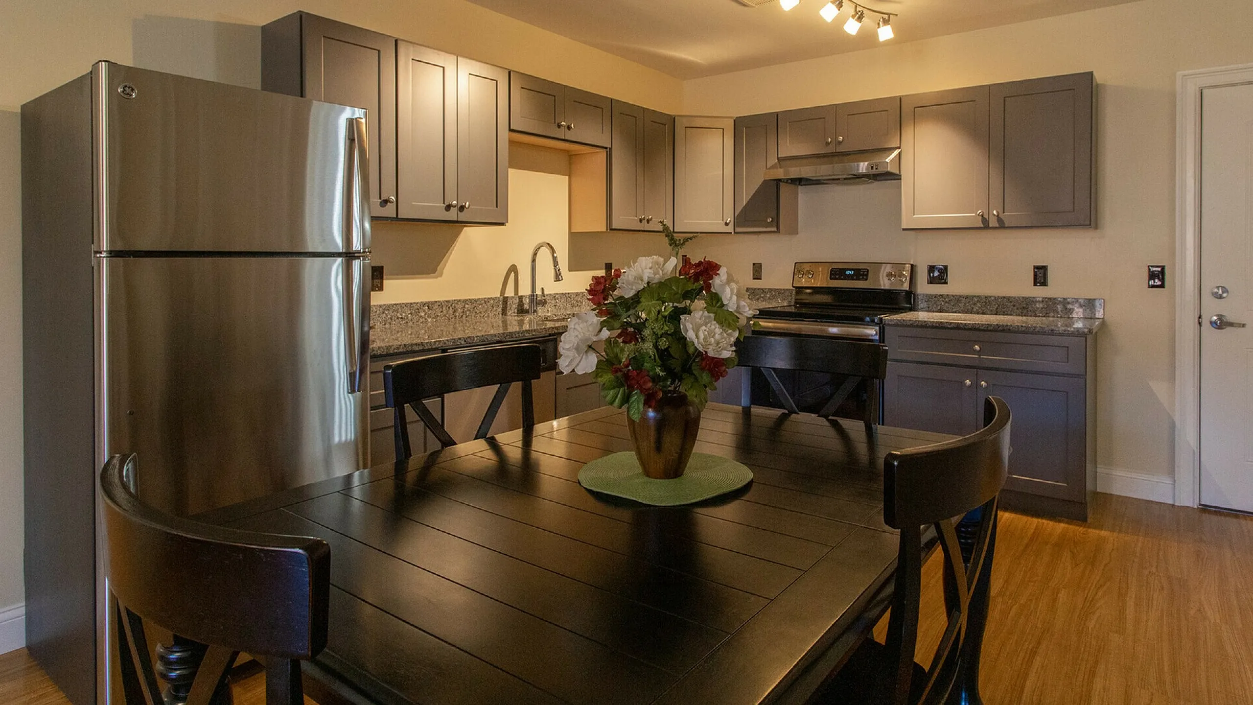 Modern kitchen featuring sleek stainless steel appliances, elegant dark wood dining table, and sophisticated granite countertops.