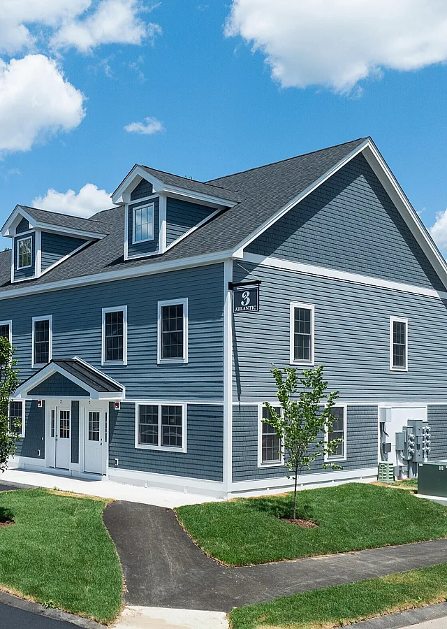 Charming multi-unit townhouse with modern blue siding, surrounded by lush greenery and a clear blue sky.