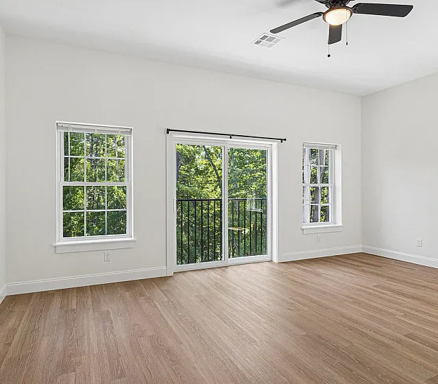 Bright and airy room with hardwood floors, large windows, and a balcony overlooking lush greenery.