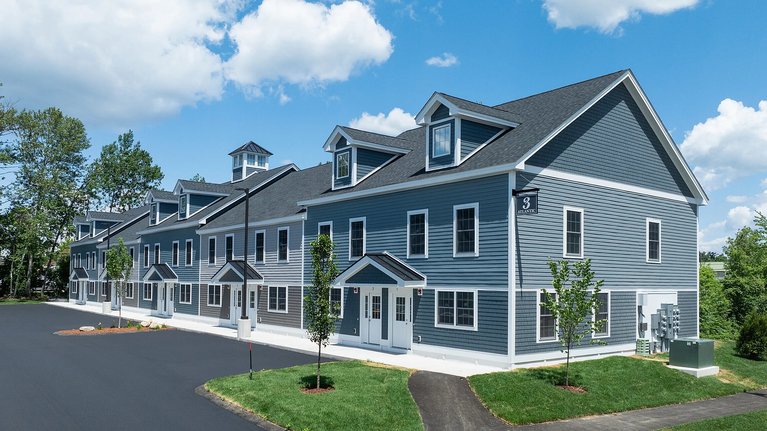 Charming blue siding apartment building with elegant dormer windows, set against a clear sky, offering a peaceful suburban atmosphere.