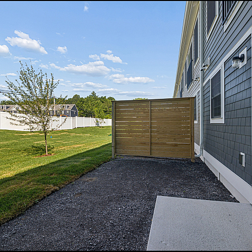 Charming backyard view with lush green grass, a neat wooden fence, and a cozy patio area, perfect for outdoor relaxation.