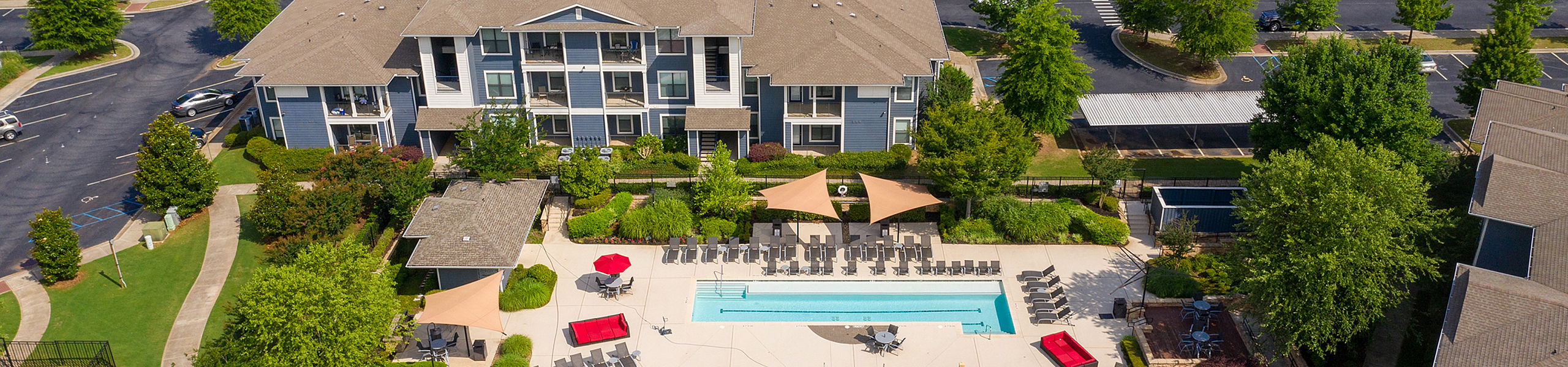 Aerial view of a luxury apartment complex with a modern design, featuring a sparkling pool, ample lounge seating, and lush greenery, offering a resort-like atmosphere.