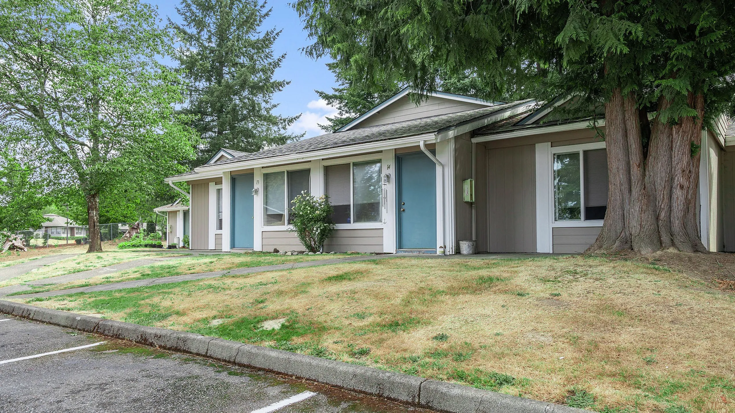 Charming single-story apartment with blue doors, nestled in a lush, green environment with picturesque trees.