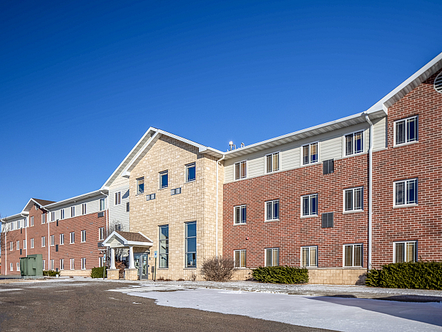 Charming brick apartment complex with a modern entrance under a clear blue sky, offering a warm and welcoming atmosphere.