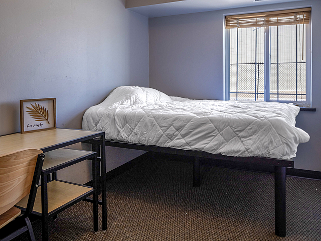 Cozy bedroom with minimalist design, featuring a raised bed next to a large window and a sleek desk and chair set.