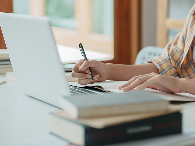 Cozy workspace featuring a modern laptop and a stack of books, perfect for productive study sessions in a bright and airy environment.