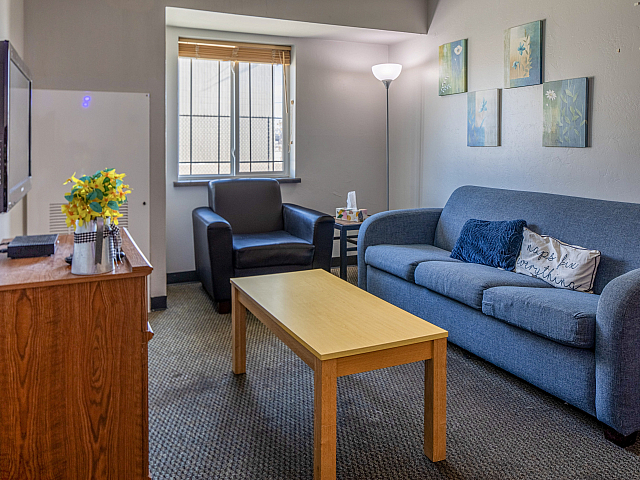 Cozy living room with modern decor featuring a comfortable blue sofa, armchair, wooden coffee table, and wall art, basked in natural light from a large window.