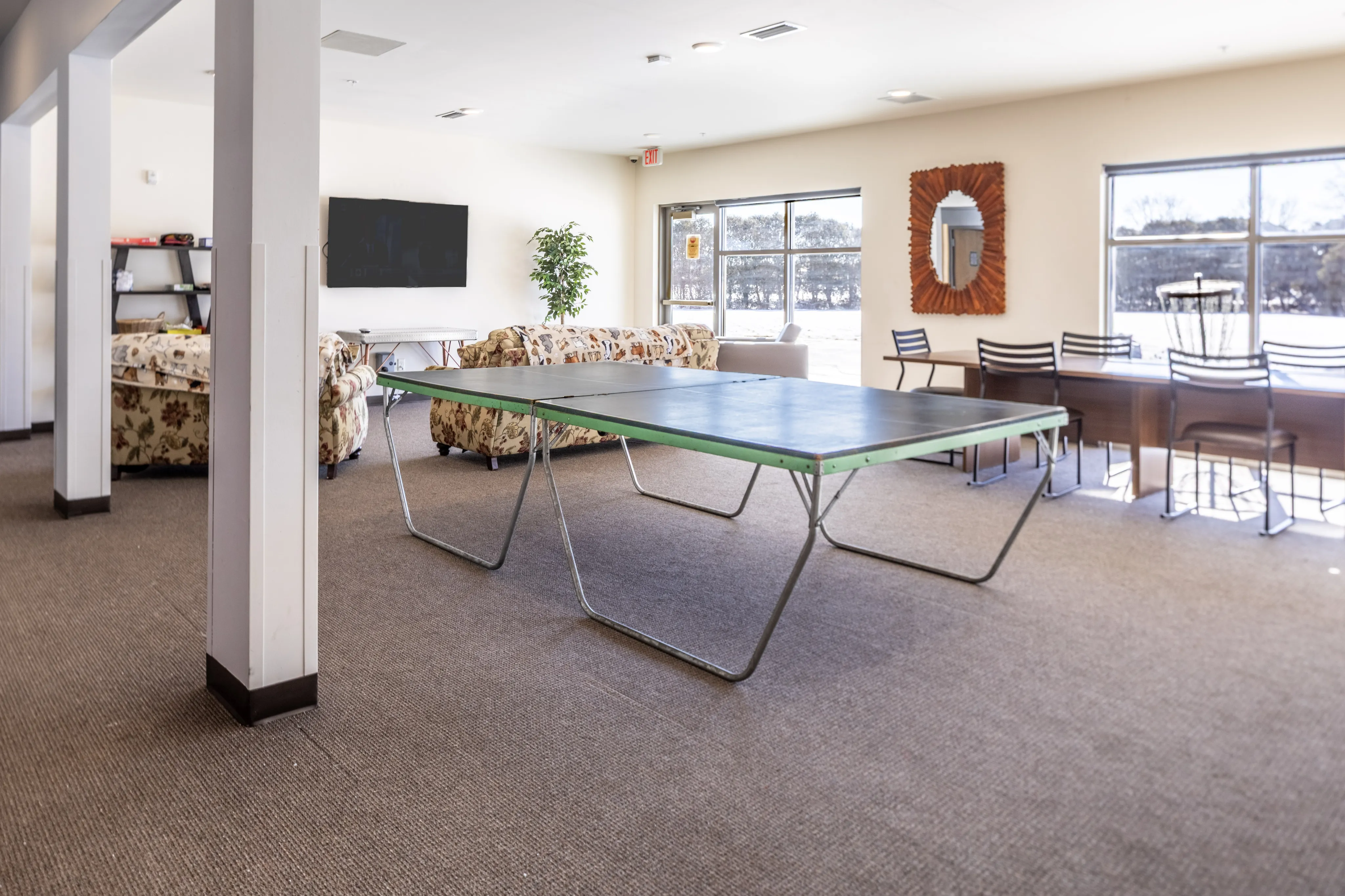 Spacious community lounge with comfortable seating, a ping pong table, and large windows offering natural light.