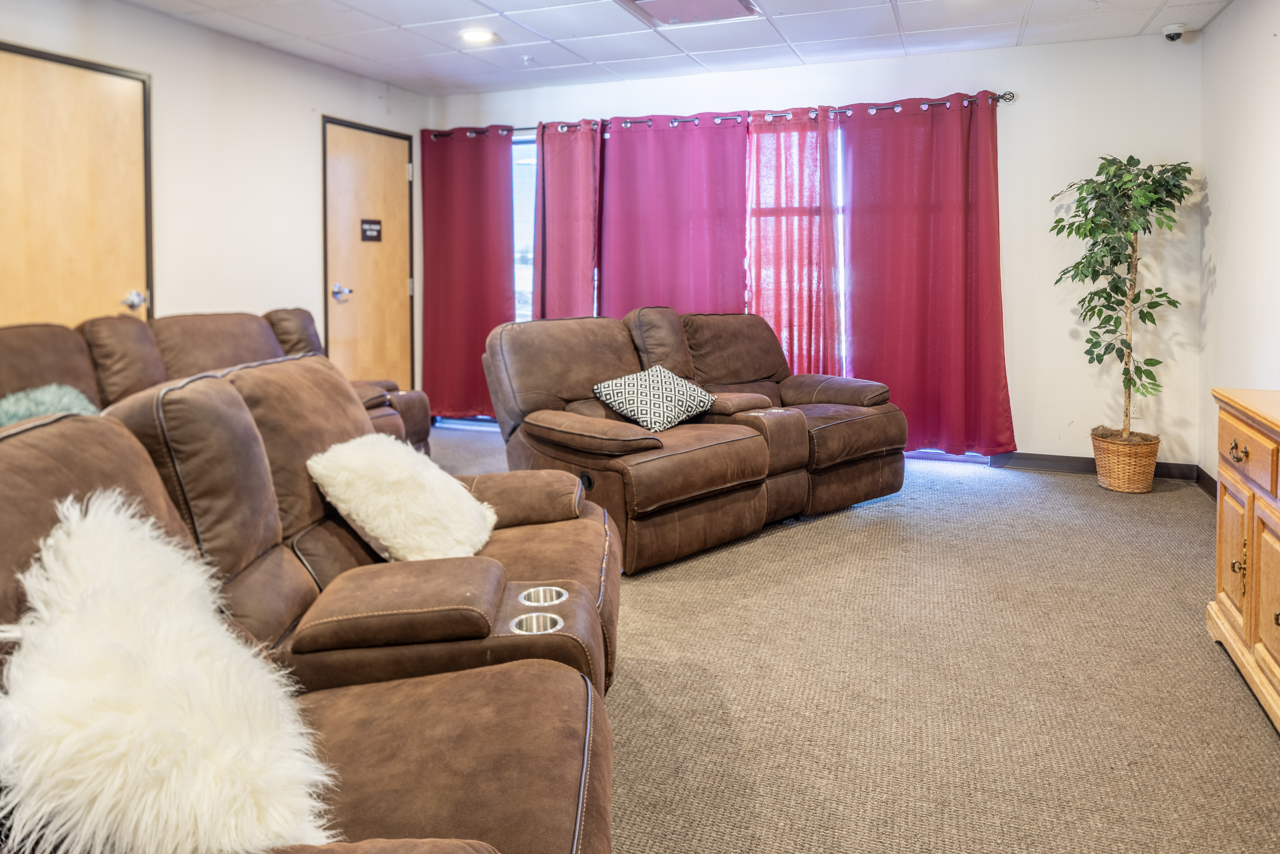 Inviting living room with plush brown sofas, red curtains, and a potted plant creating a warm ambiance.