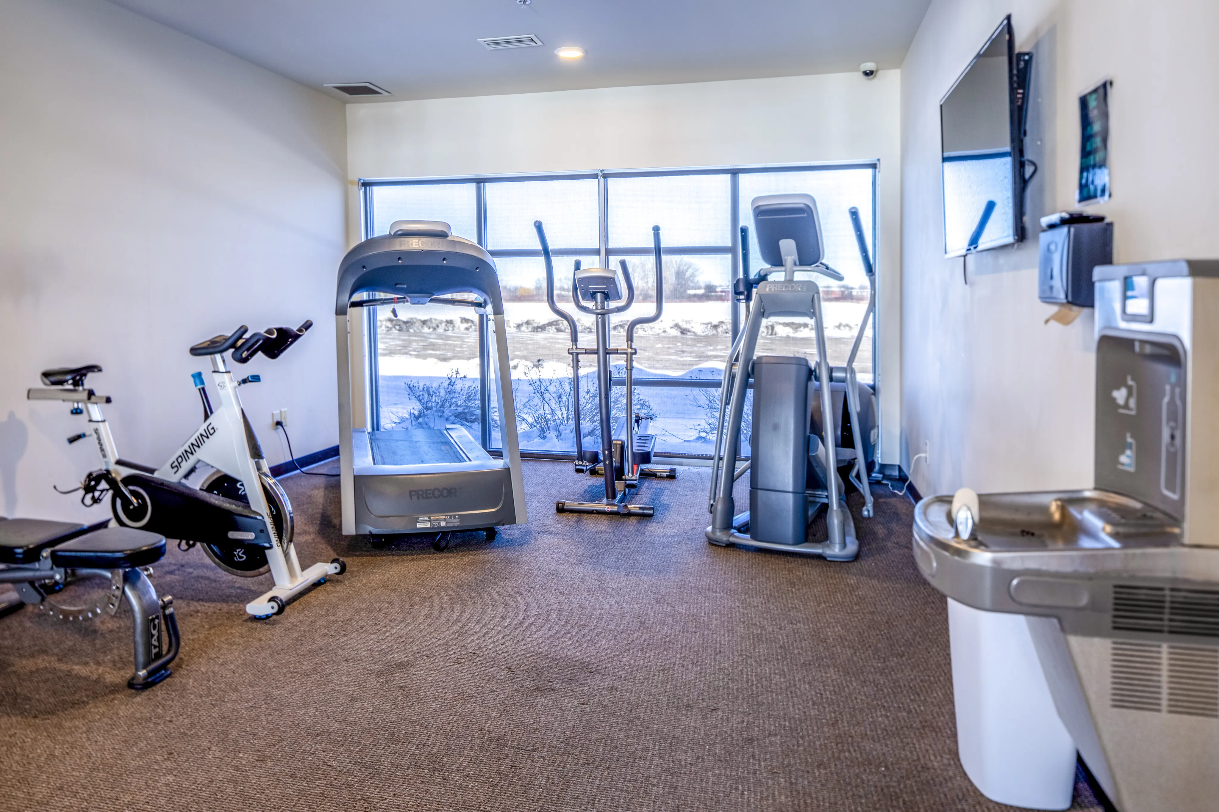 Bright gym space featuring modern exercise equipment, including spin bike, treadmill, and elliptical.