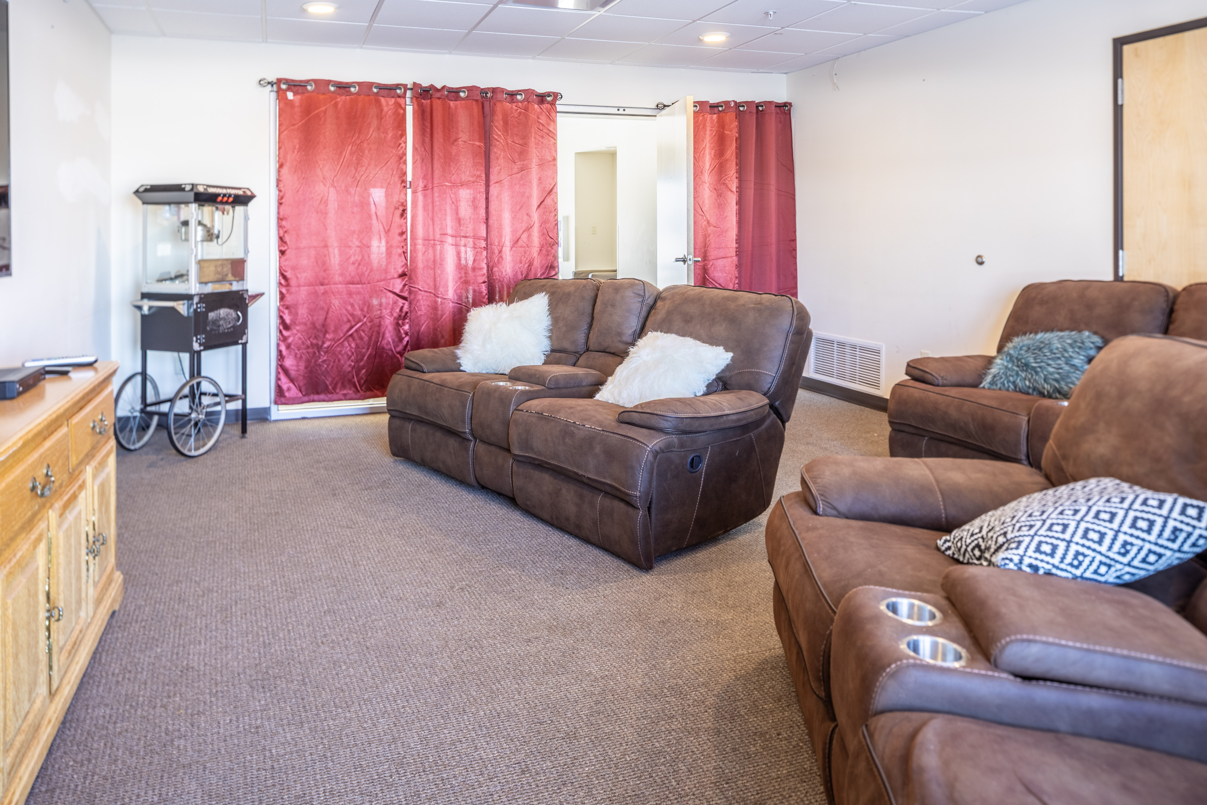 Inviting living room with plush brown seating, vibrant red curtains, and a popcorn machine.