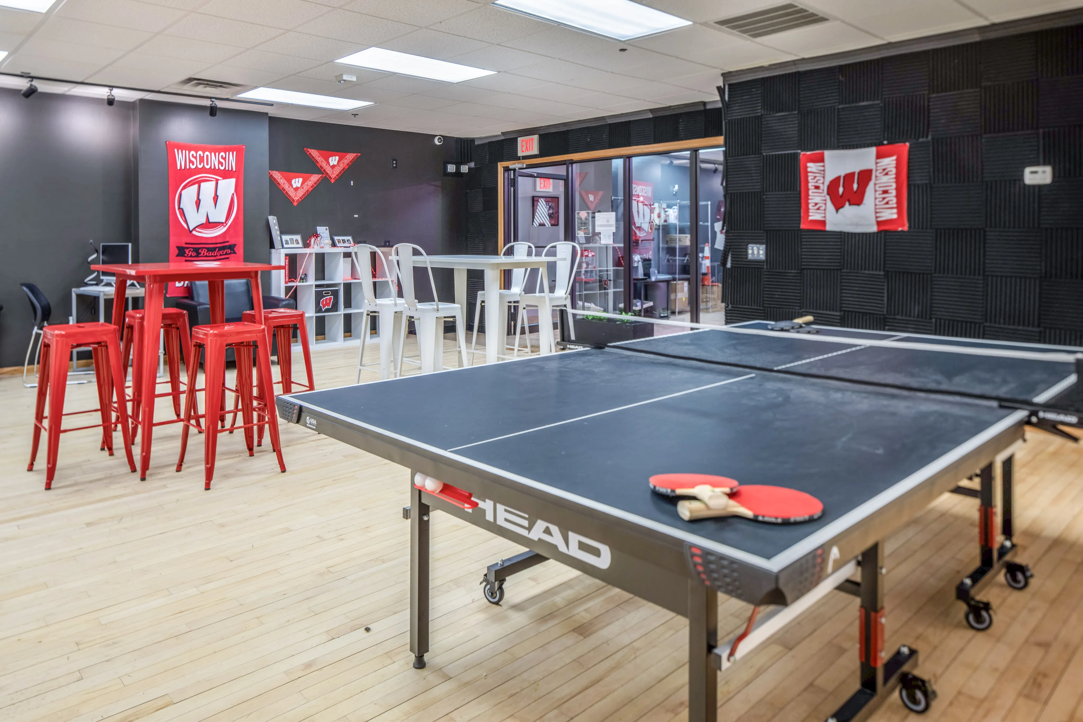 Dynamic lounge area featuring a ping pong table, vibrant red stools, and a modern study nook with Wisconsin decor.