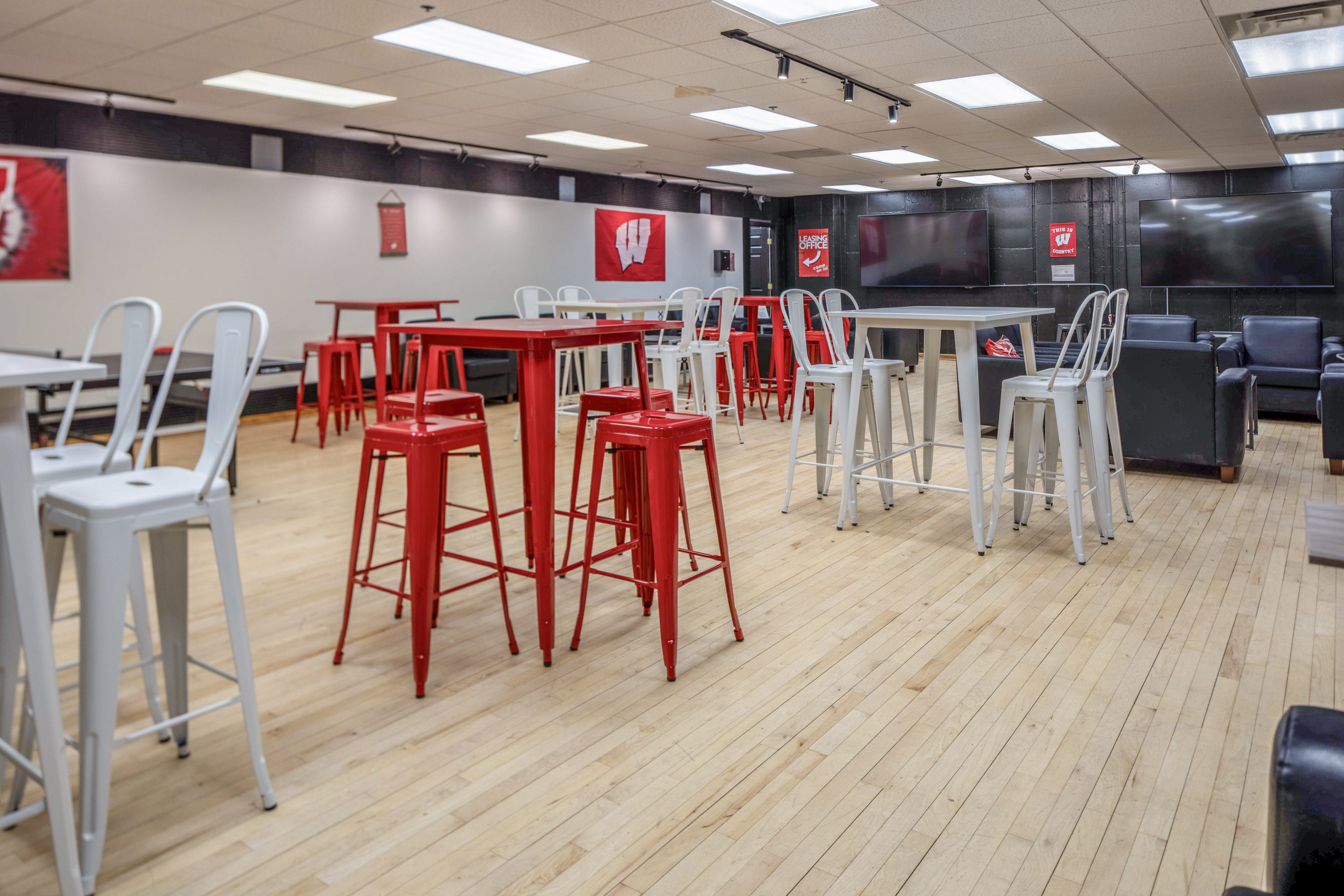 Inviting social lounge with red and white high tables and stools on a polished wooden floor.
