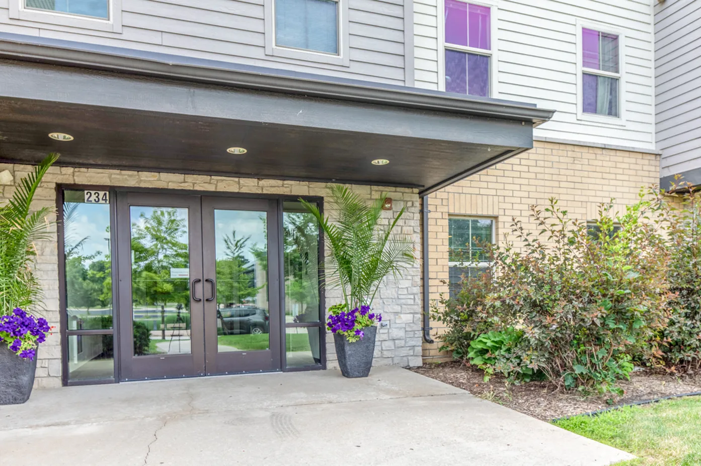 Inviting apartment entrance with modern glass doors, vibrant potted plants, and well-maintained landscaping.