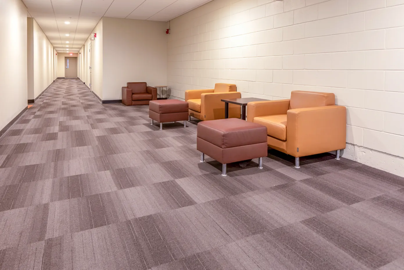 Inviting apartment hallway with cozy seating area featuring modern leather chairs and a plush carpet design.