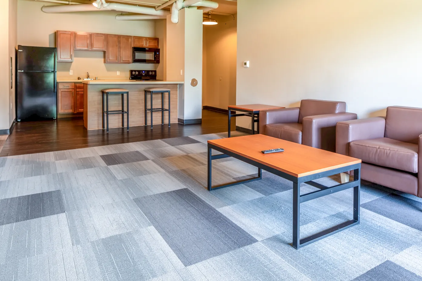 Modern open-plan living space with cozy seating, elegant kitchen, and stylish bar stools on a chic patterned carpet.