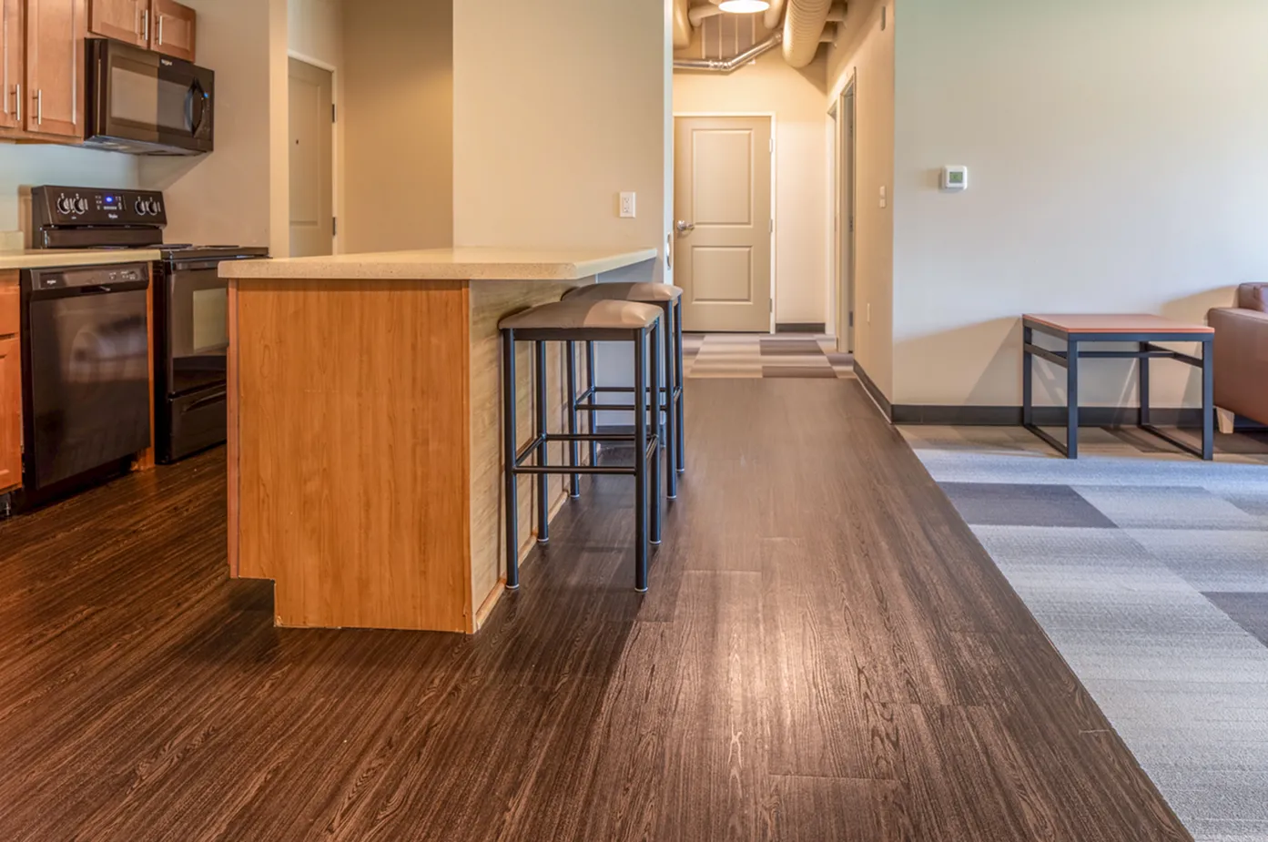 Modern kitchen with sleek wooden cabinetry, stylish countertops, and inviting bar seating, leading into a cozy open living area.