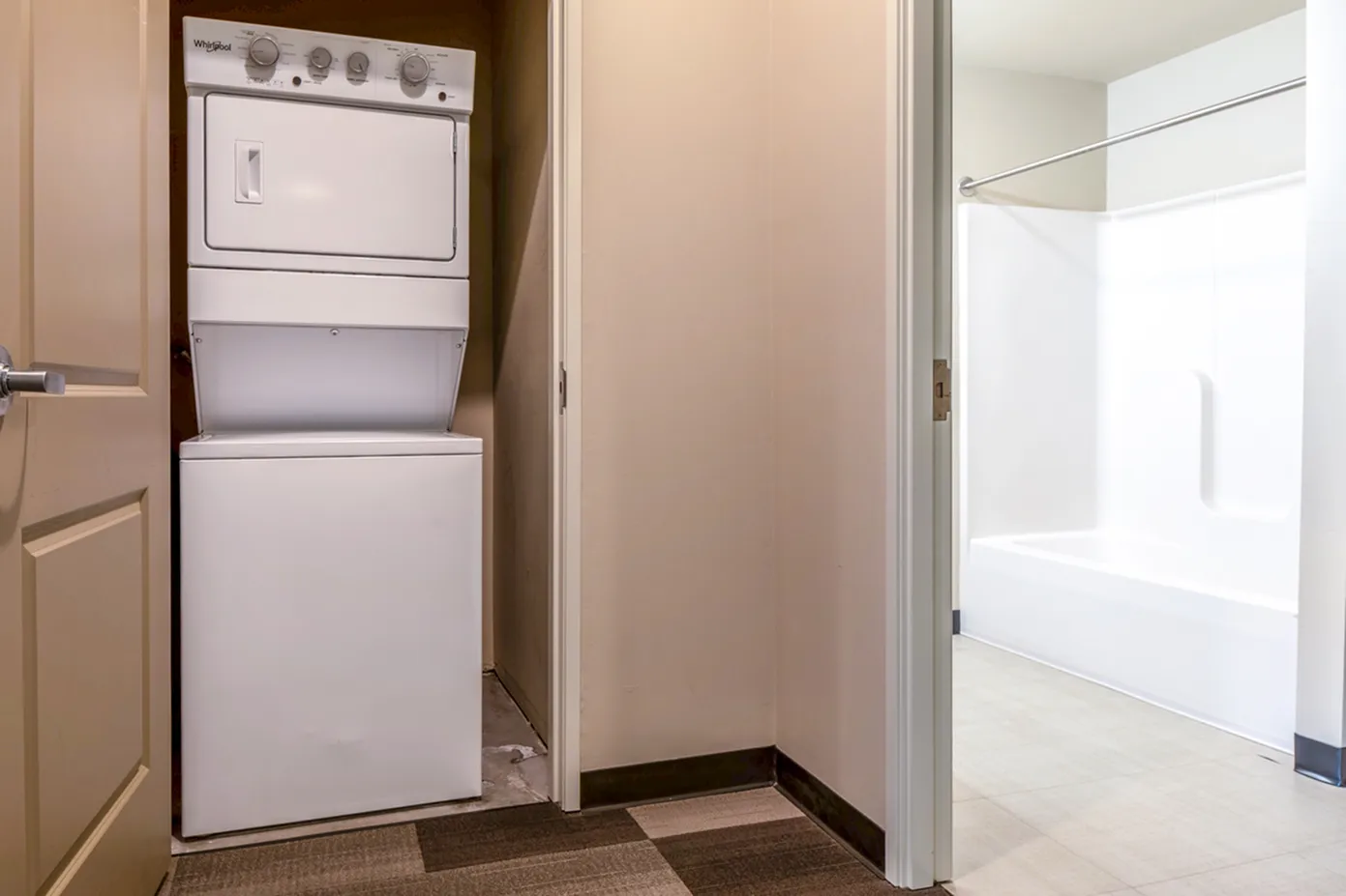 Modern apartment showcasing in-unit laundry with a sleek stackable washer-dryer set and an adjacent bright bathroom featuring a roomy bathtub.